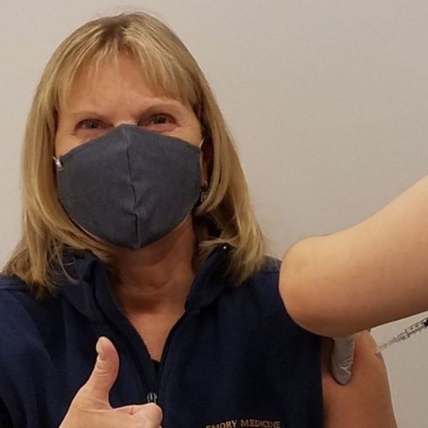 A woman in a face mask gives a thumbs up while getting vaccinated